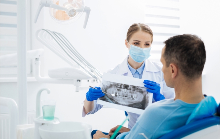 A dentist pointing to and explaining the results of an x-ray that was performed for her patient