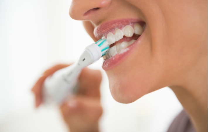 A close up of a woman's mouth while shes using an electric toothbrush to clean her teeth