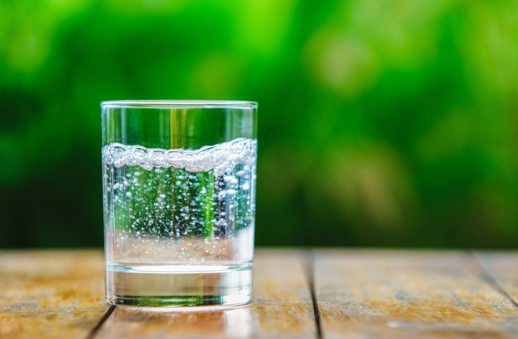 A glass of sparkling water placed on a wooden surface with a blurred, green, outdoor background