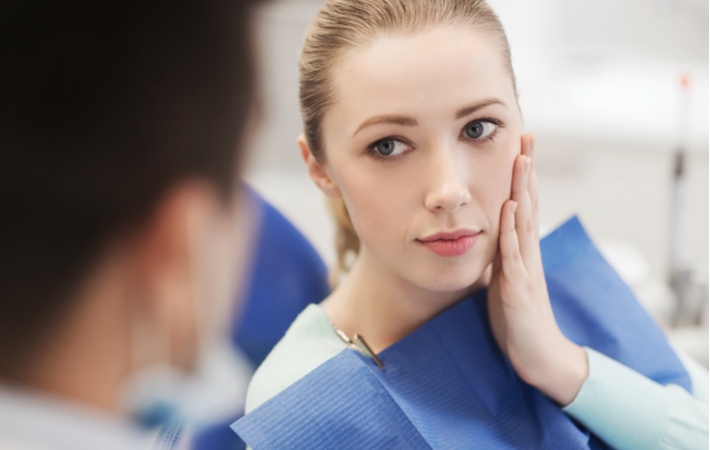 A woman visiting her dentist as she holds her cheek in the dentist's chair due to a dental crown that has fallen out