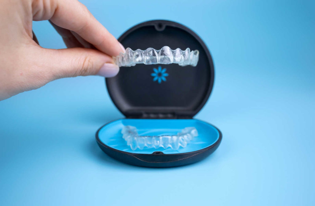 A hand putting Invisalign clear aligners in their protective case while they aren't being worn to prevent damage