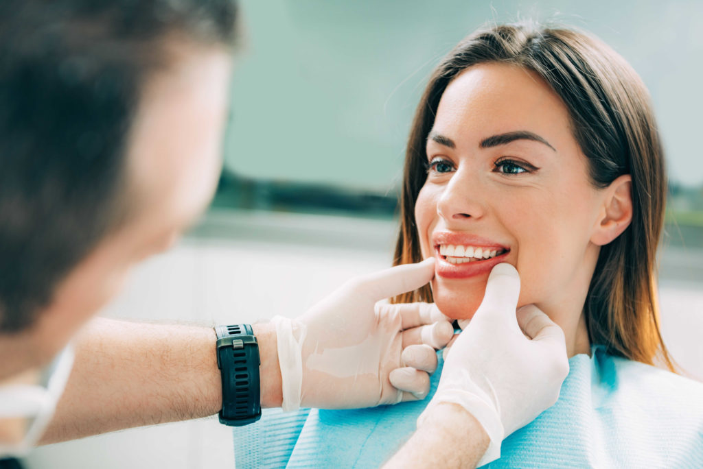 A patient at a dental exam having her teeth examined by the dentist to monitor her cosmetic dentistry treatment progress