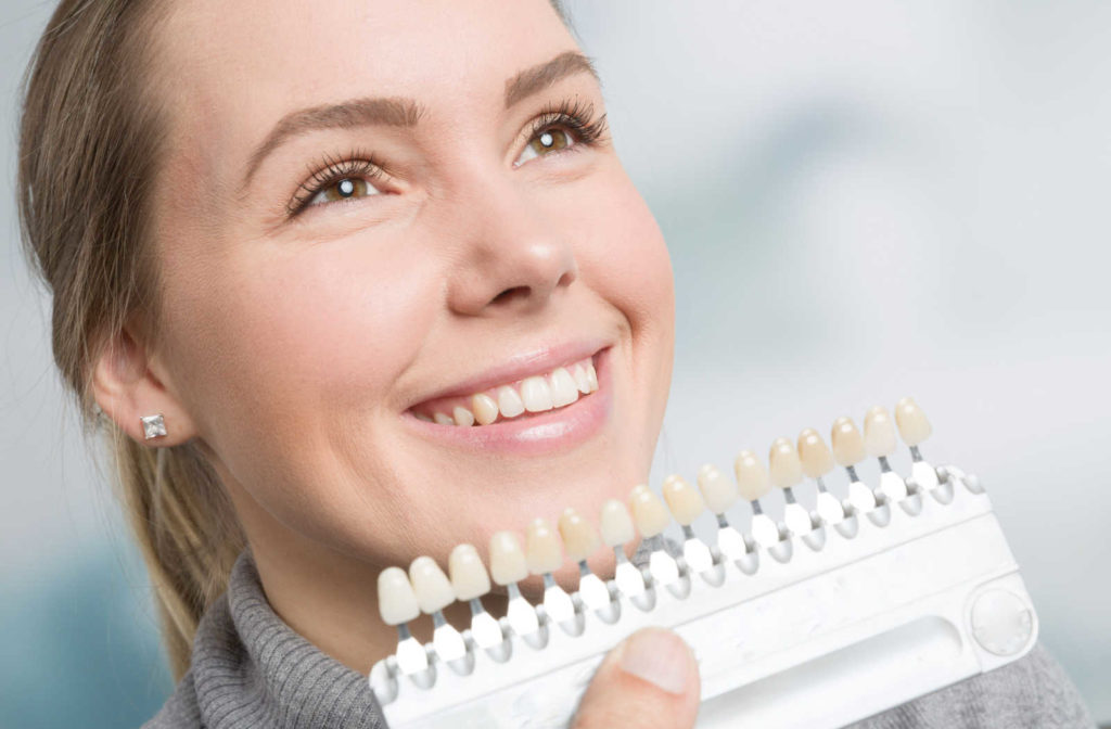 A patient smiling while a dentist uses a shade guide during an in-office teeth whitening treatment
