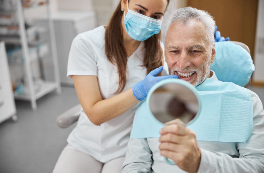 A dental patient looking in the mirror at the end of an appointment to see the dental implant seamlessly blend in with the rest of his teeth.