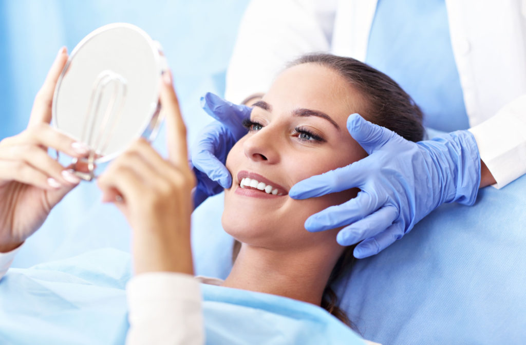 A dental patient looking in a hand-held mirror while the dentist points to either side of the patient's mouth.