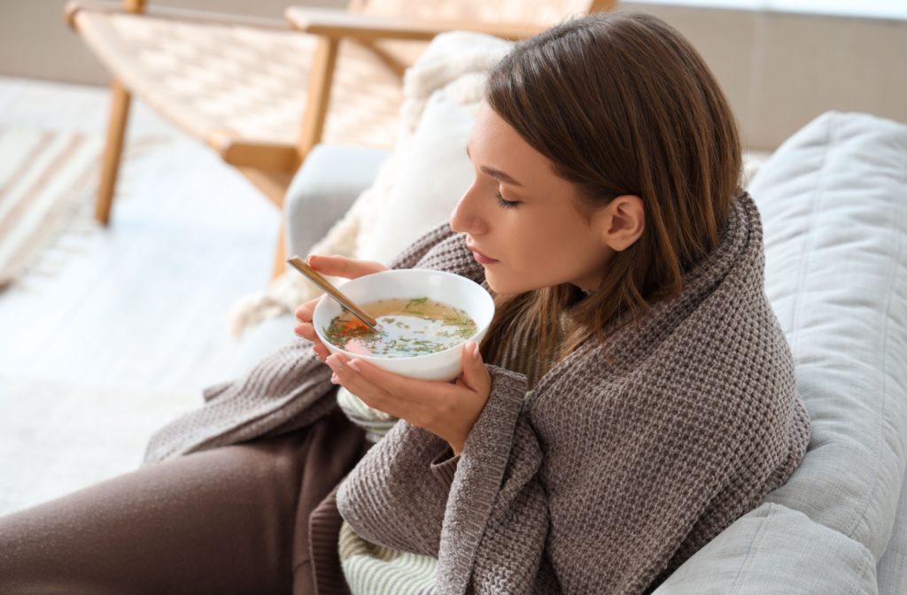 A woman sitting on the couch with a bowl of soup to eat after having a tooth extracted.