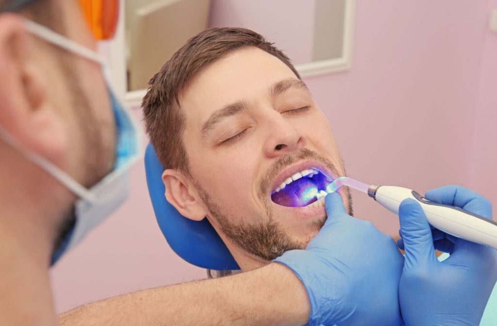A male dentist examining patient's teeth using a specialized device in a dental clinic.