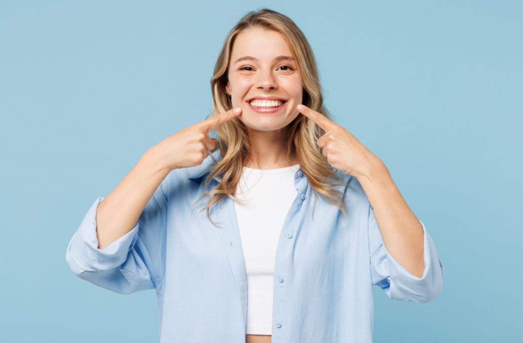 A woman smiling while pointing at her teeth to show her permanent veneers