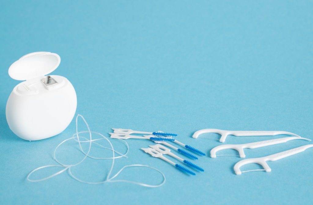 Traditional floss, floss picks, and interdental brushes on a blue surface