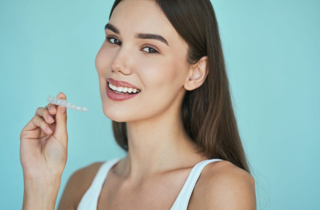 Young patient smiles while holding Invisalign clear aligners