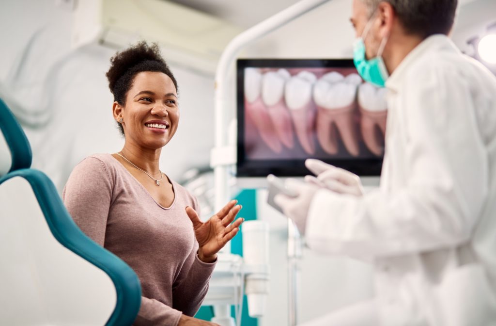 A person with a straight smile sitting in a dental chair and talking to their dentist after Invisalign treatment