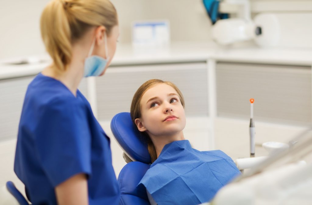 a young teenager sits on a dental chair, talking to their dentist regarding an oral health evaluation and Invisalign consultation