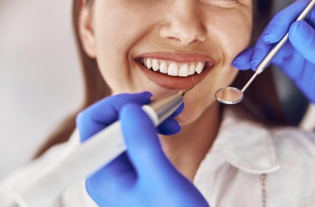 A patient smiling while an out-of-frame dentist carefully cleans between their teeth during a professional cleaning.