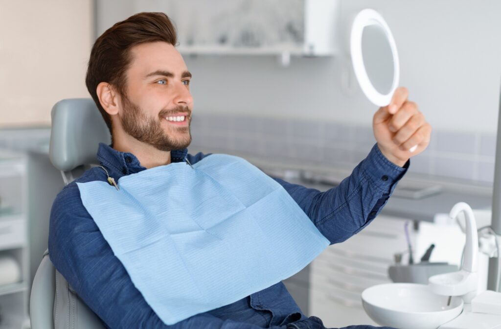 A patient smiling in a handheld mirror after their dental exam to restore their chipped tooth.