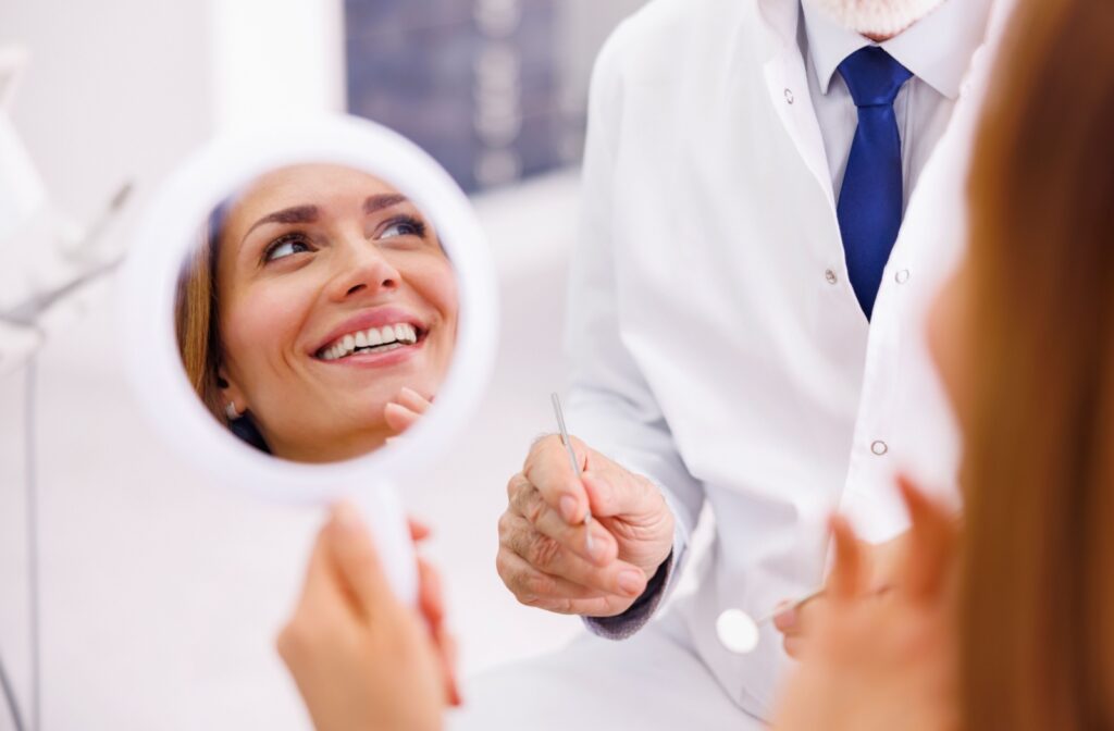 A women at the dentist holding a mirror so she can see her smile with no gaps after getting the gaps fixed with dental bonding.