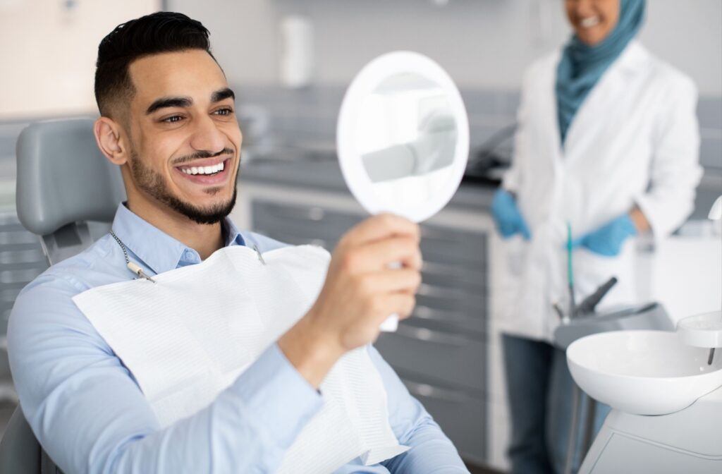 A young male at the dentist, smiling in a handheld mirror.