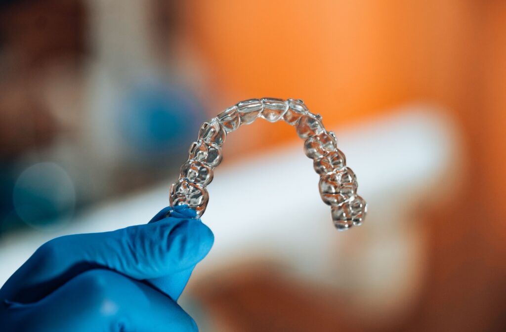 A hand wearing a blue surgical glove, holding an Invisalign clear aligner.