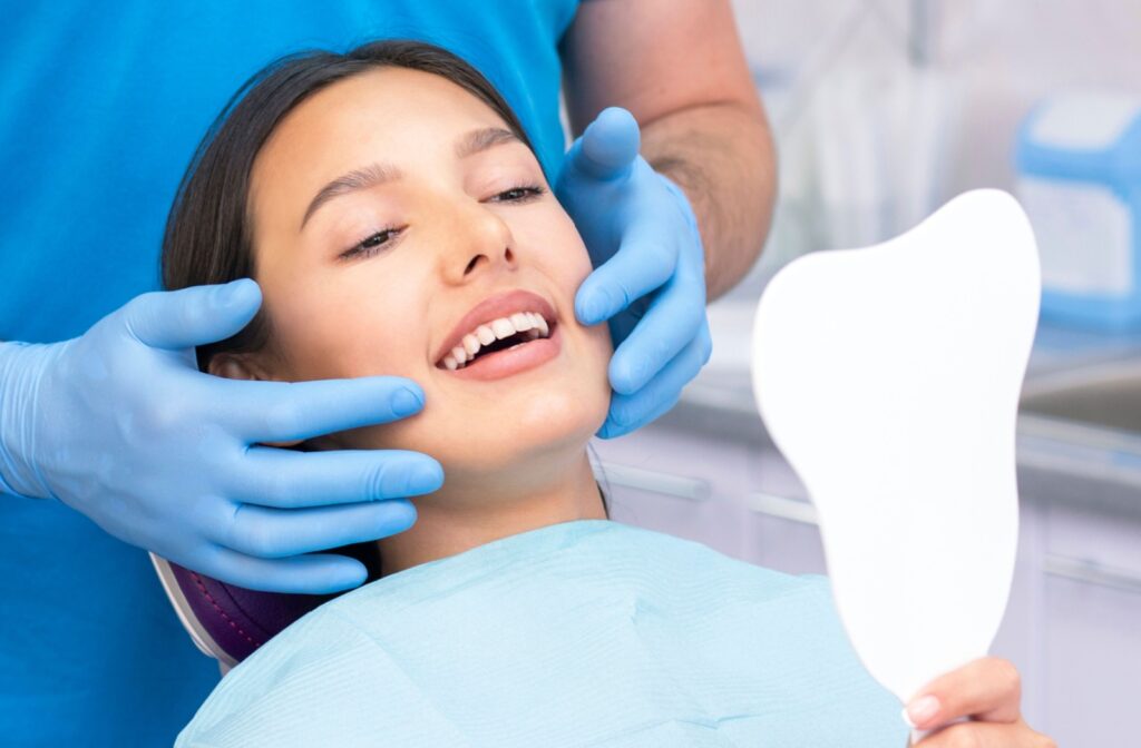 A patient at the dentist looking in a handheld mirror after a consultation to straighten crooked bottom teeth.